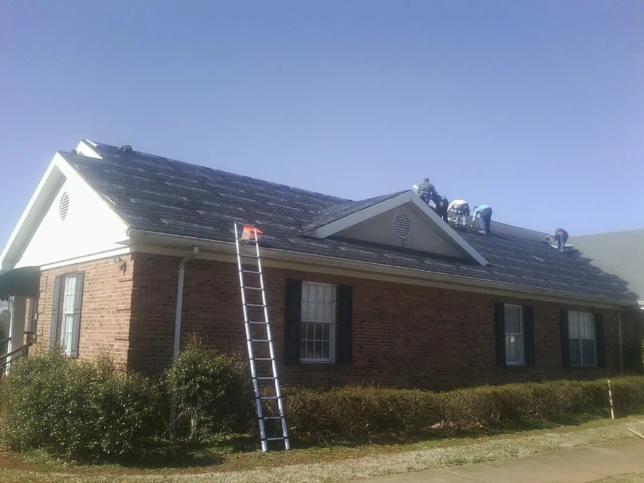Crew tearing shingles off a brick ranch roof with a ladder set — Metal Roof Repair work by our crew in Autryville
