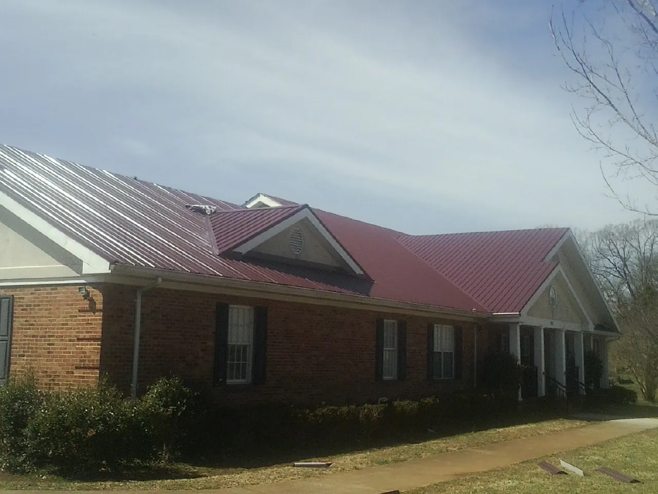 Red metal roof with gabled entries on a long brick building, from a Hail Damage Roof Repair job in Autryville