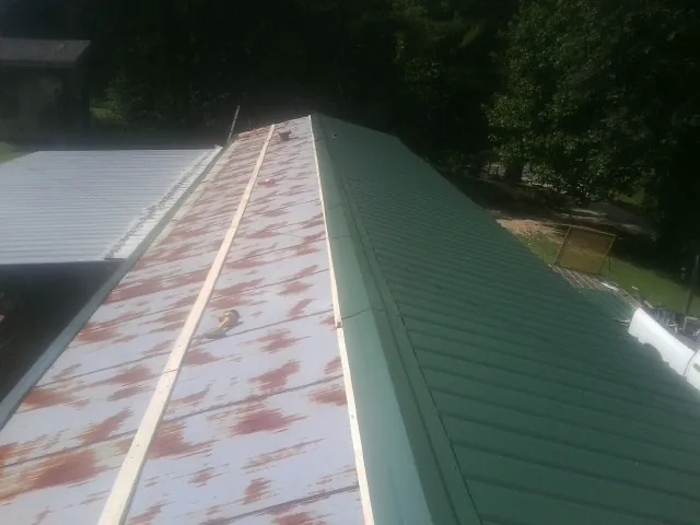 Old rusted panels beside newly installed green metal roofing — Wind Damage Roof Repair by Roofing Brothers in Autryville