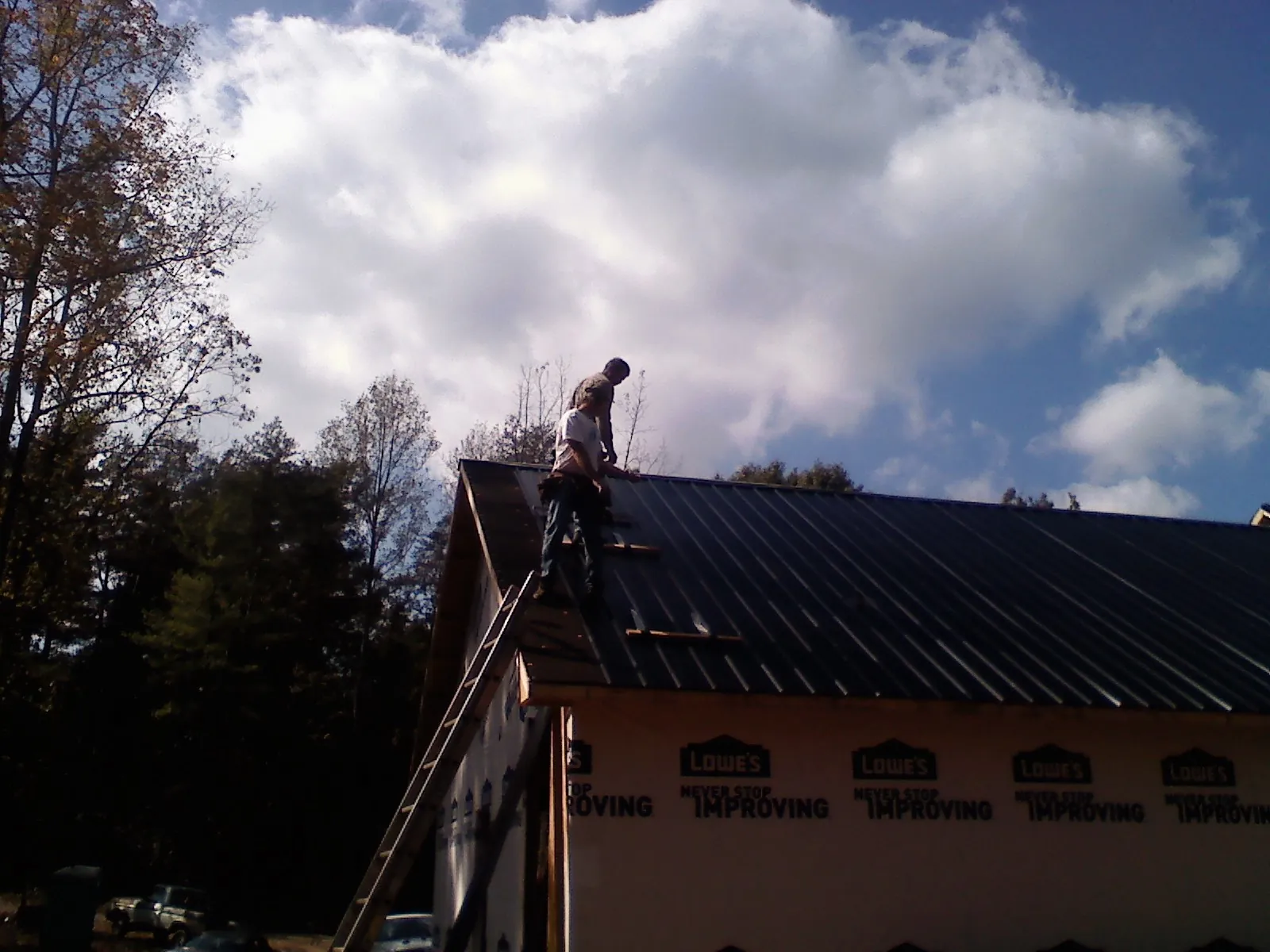 Roofer fastening dark metal panels high against a cloudy sky, from a Roof Inspection job in Autryville