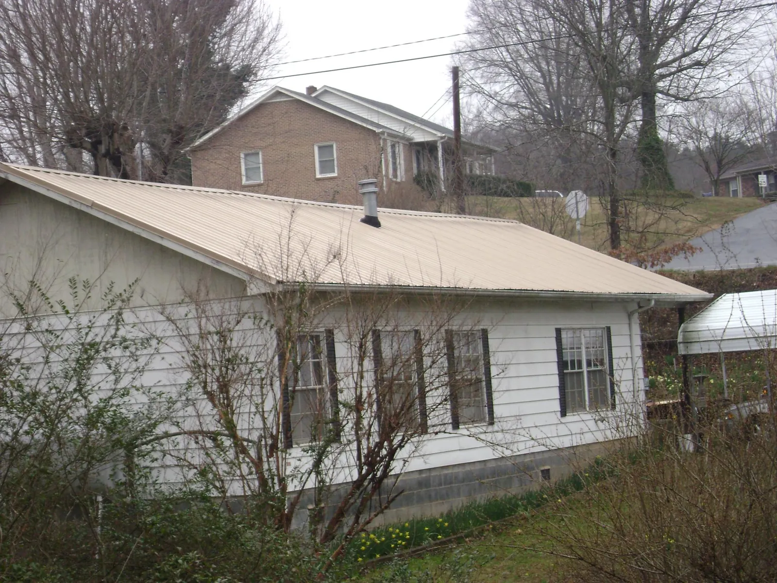 Tan metal roof on a white sided house set into a hillside — Commercial Roofing by Roofing Brothers in Autryville