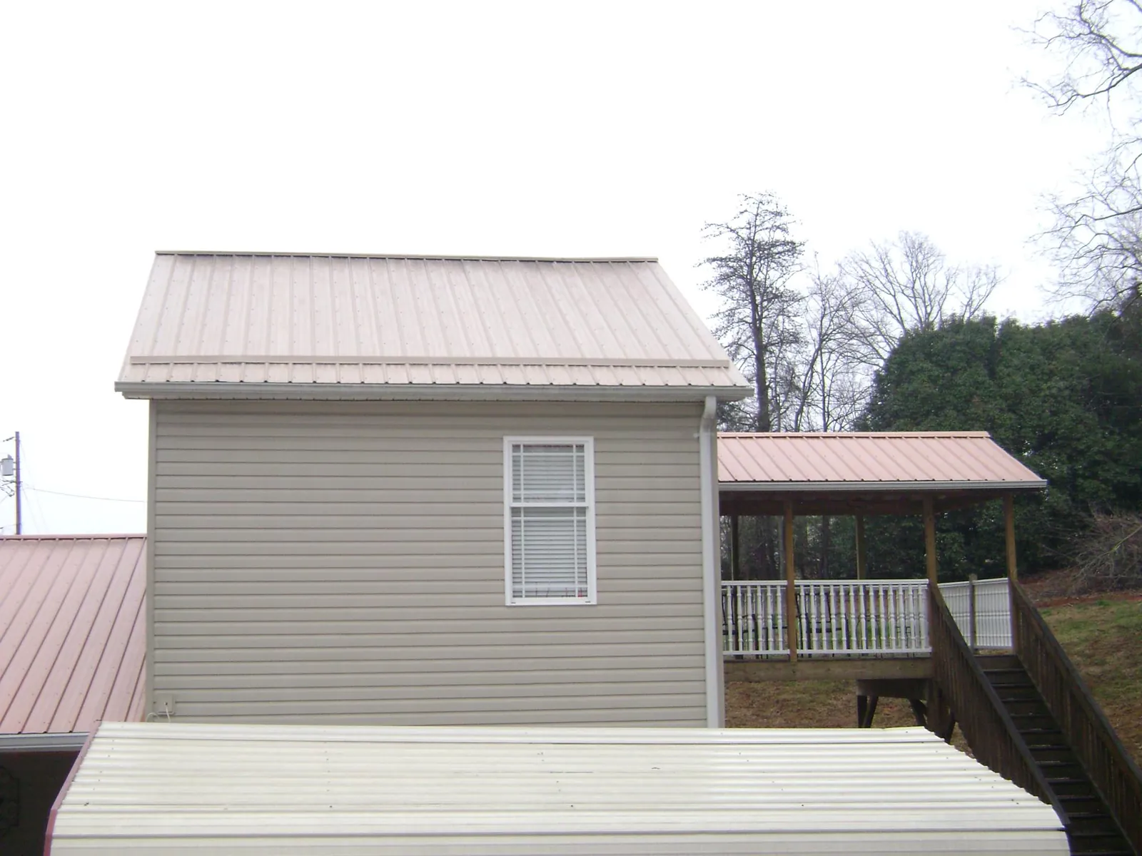 Tan metal roofs on a two story addition and attached porch, from a Roof Replacement job in Autryville